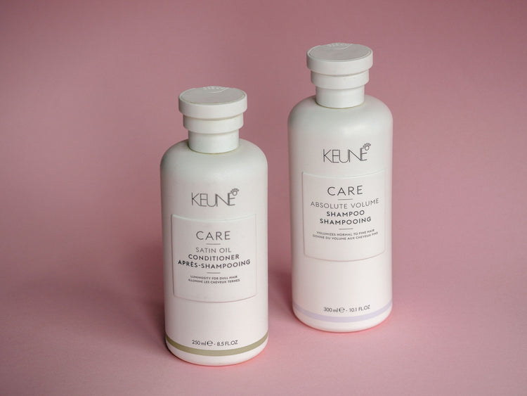 White Keune shampoo and conditioner bottles on a soft pink background.
